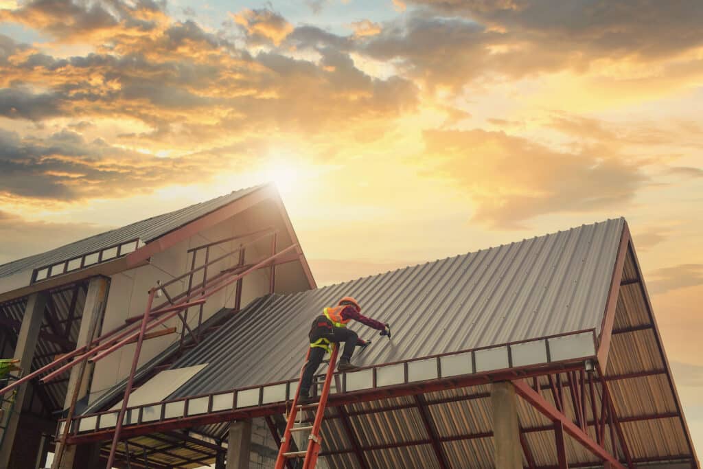roofing companies in denver installing a tall metal roof during the sunset