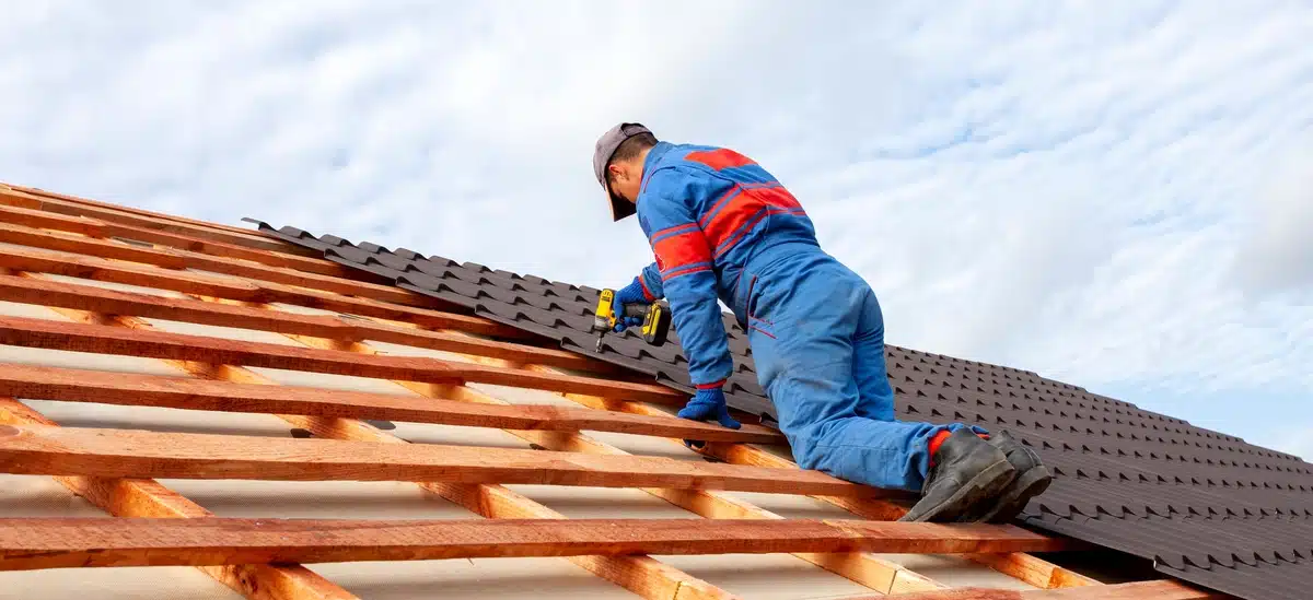 professional worker using drill to install new tiles on roof