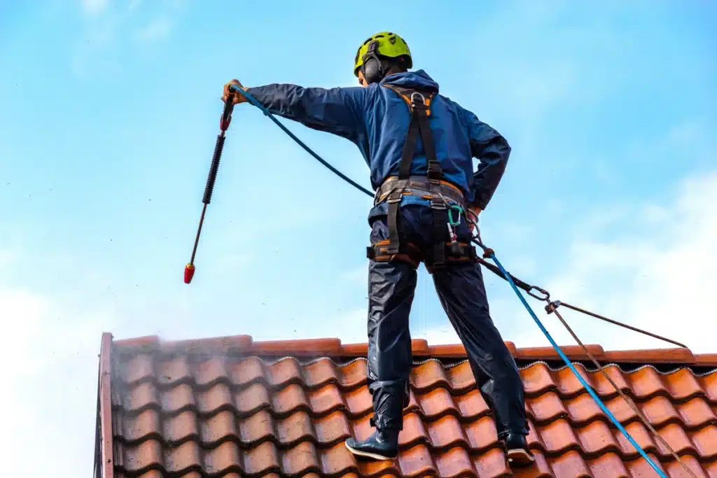 worker washing the commercial roof wearing safety gear
