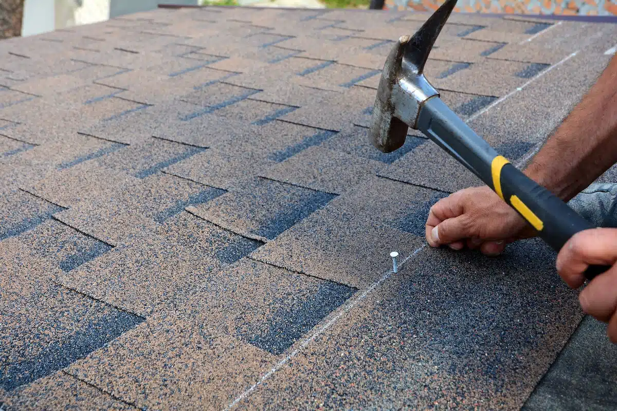 close up of brown asphalt roofing shingles being nailed to roof
