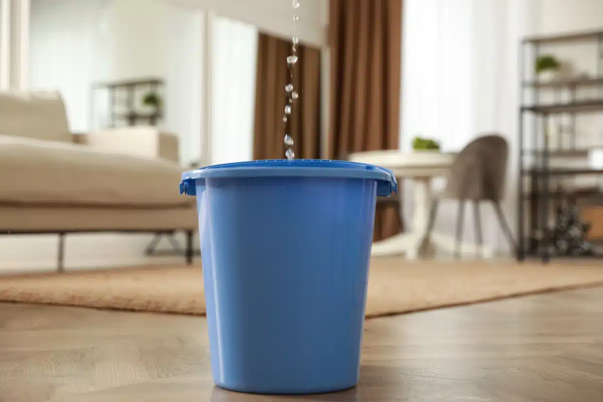 A ceiling leak drips into a blue bucket