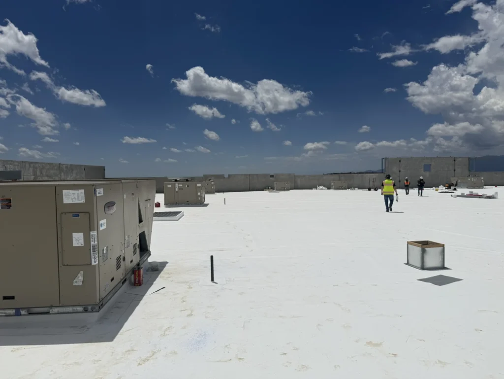 Commercial white membrane roof with rooftop units and crew members in the distance